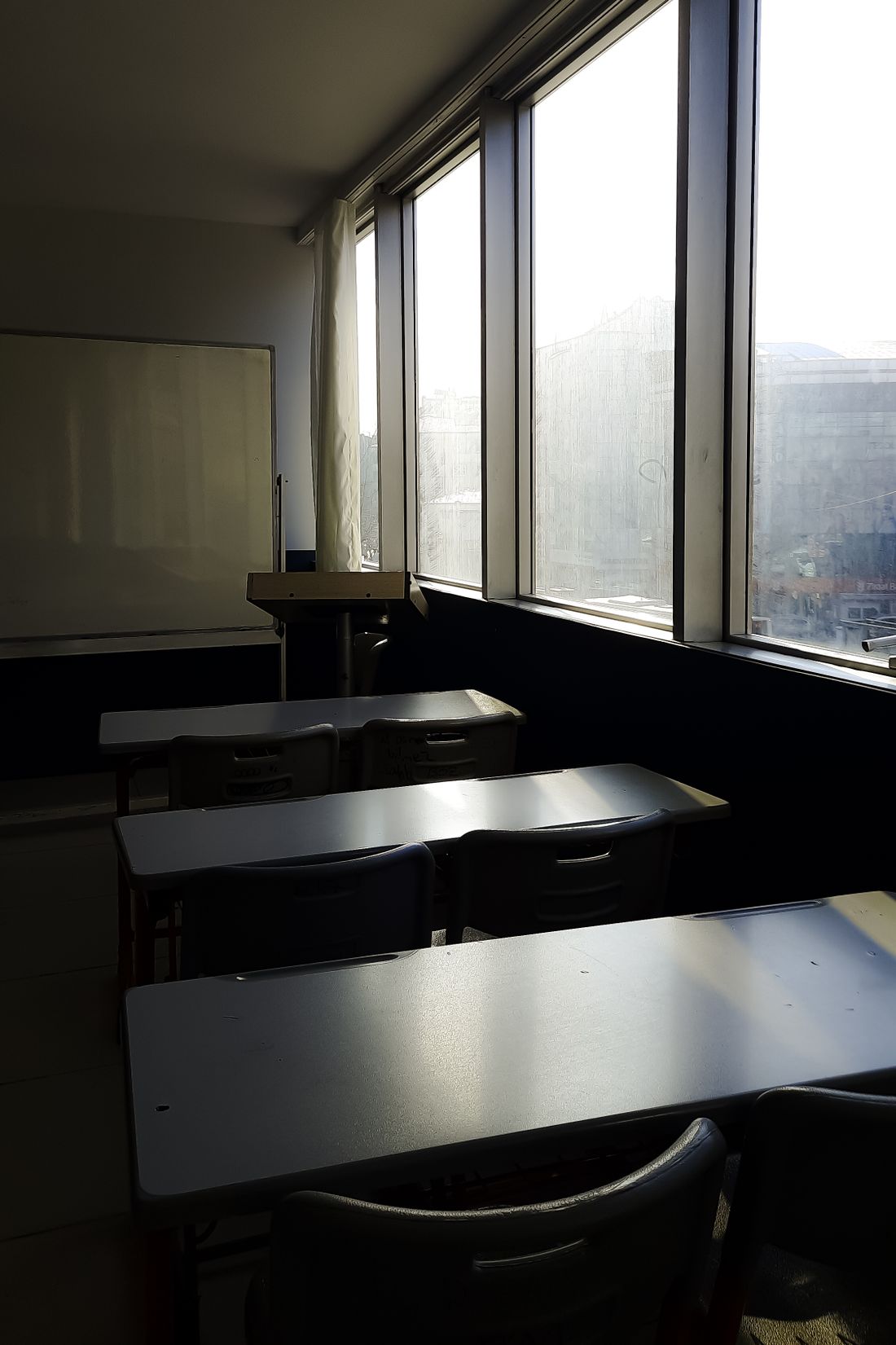 An empty classroom with a wall of windows, bright light flooding in across rows of unoccupied desks