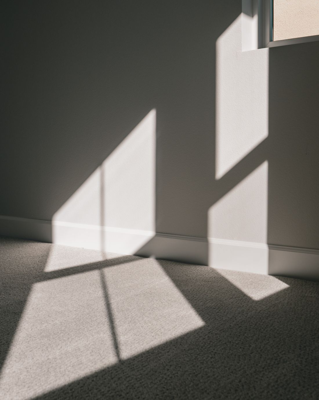 A hard-edged patch of window light on the wall and carpet of an empty room